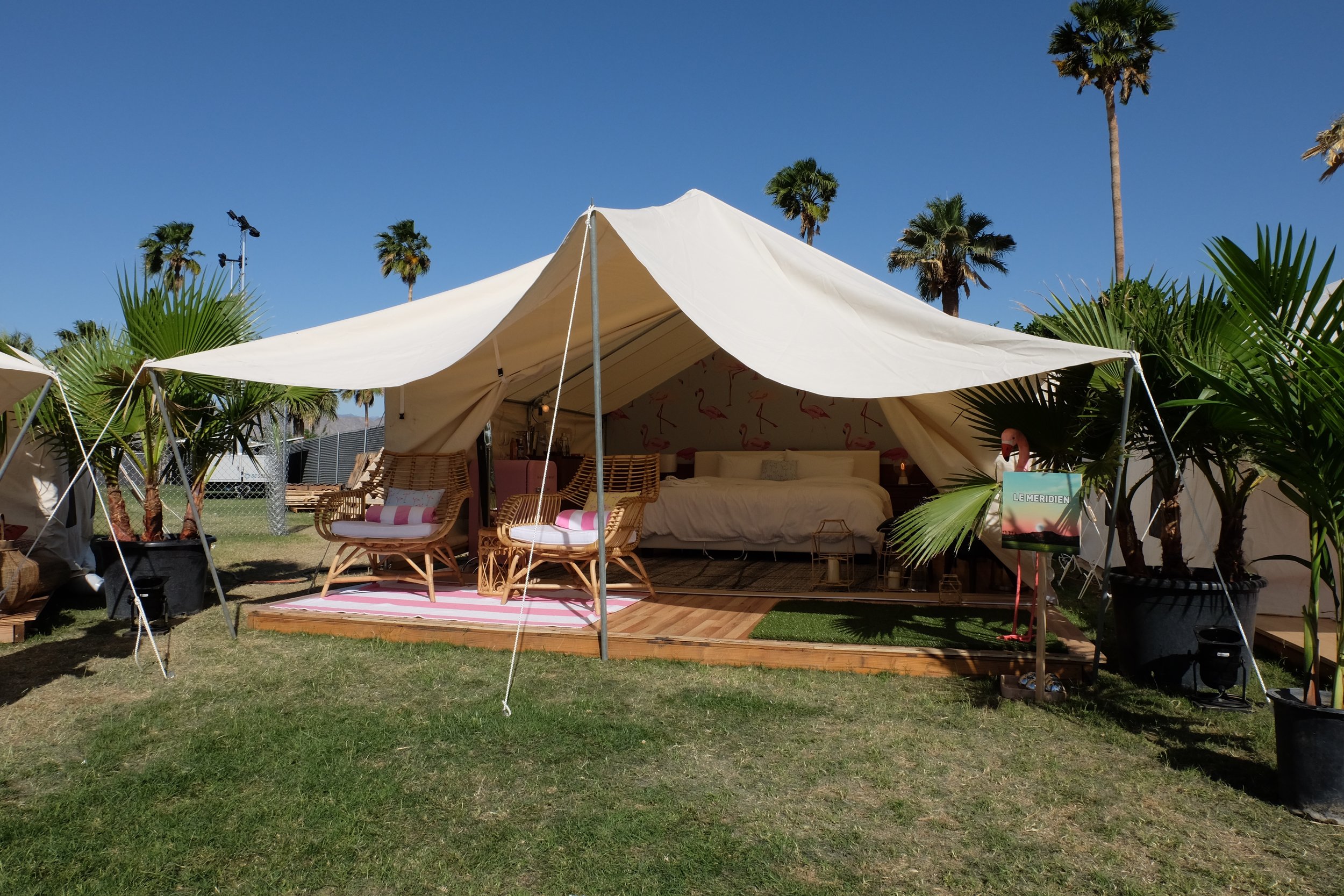 Image of an open tent with a bed and two chairs underneath and a flamingo wallpaper behind the bed