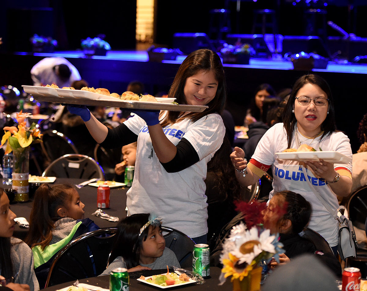 Two female AEG employees serve plates of food from a tray to families at the AEG Thanksgiving Celebration at L.A. LIVE's The Novo. 