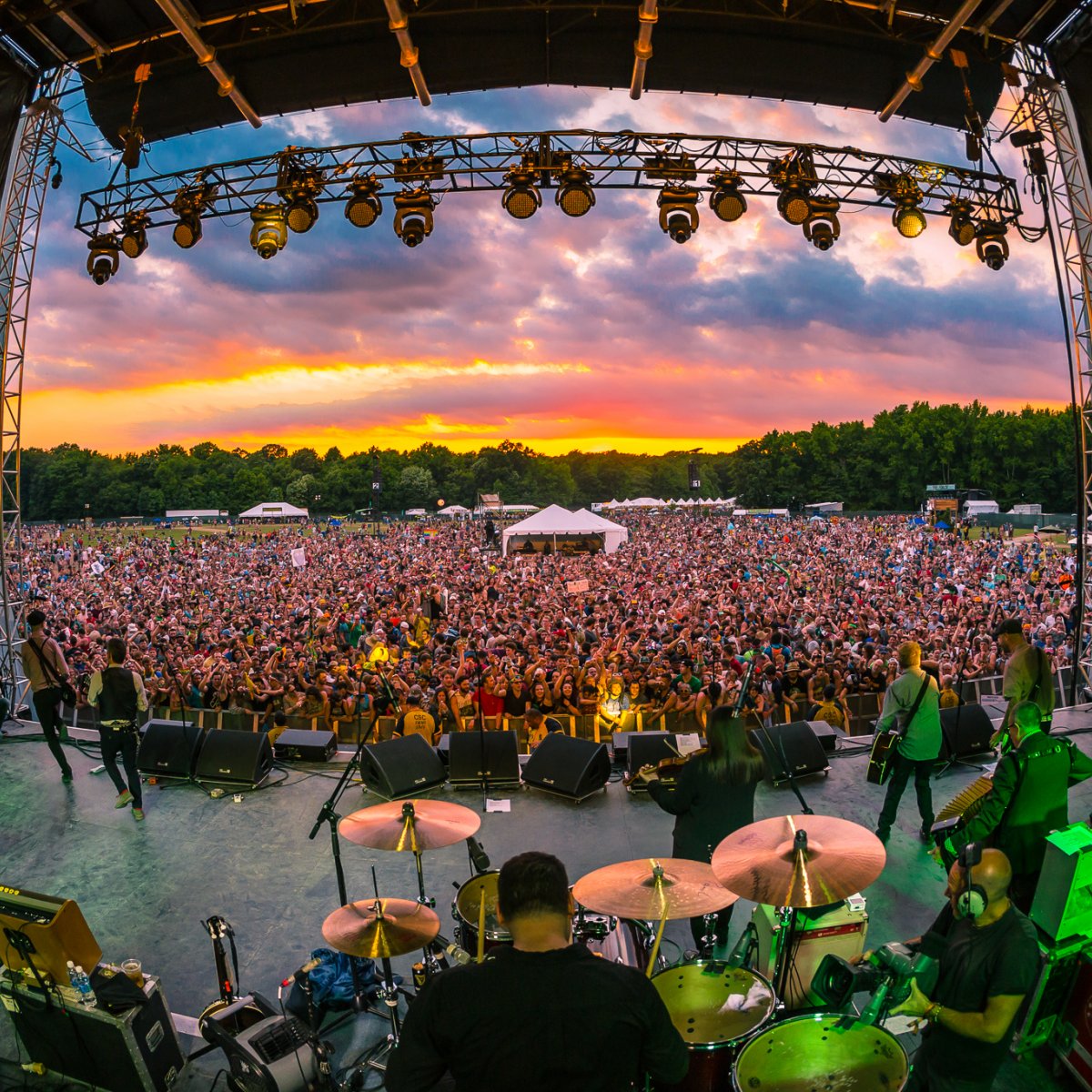 Image looking out into the crowd from behind performers on stage with a vibrant sunset at Firefly Music Festival